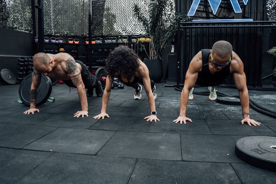 Three individuals performing push-ups together in a Mexico City gym setting.